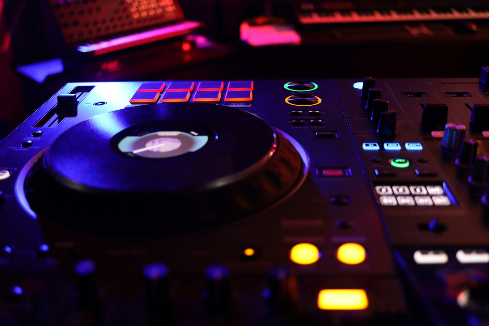 Close-up van een Pioneer-dj-set in warm oranje licht: jog-wheels, faders en de mixer in een donkere booth.